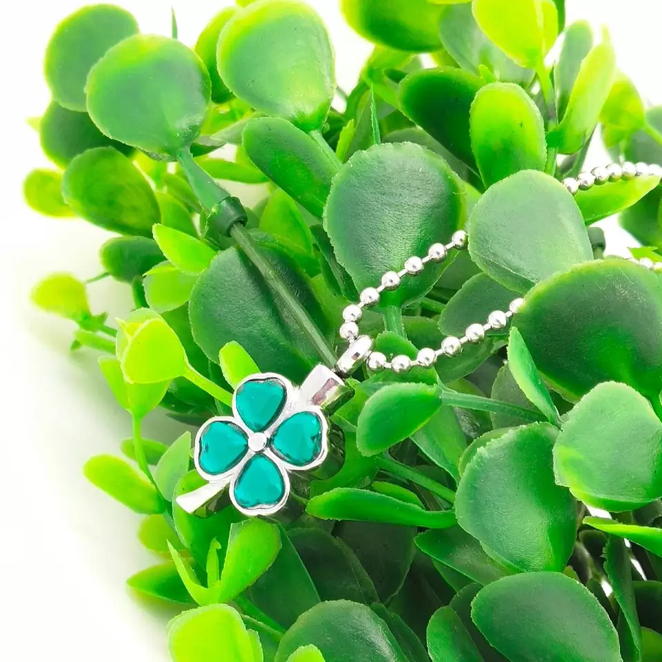 Image of a green clover cremation necklace lying on a plant.