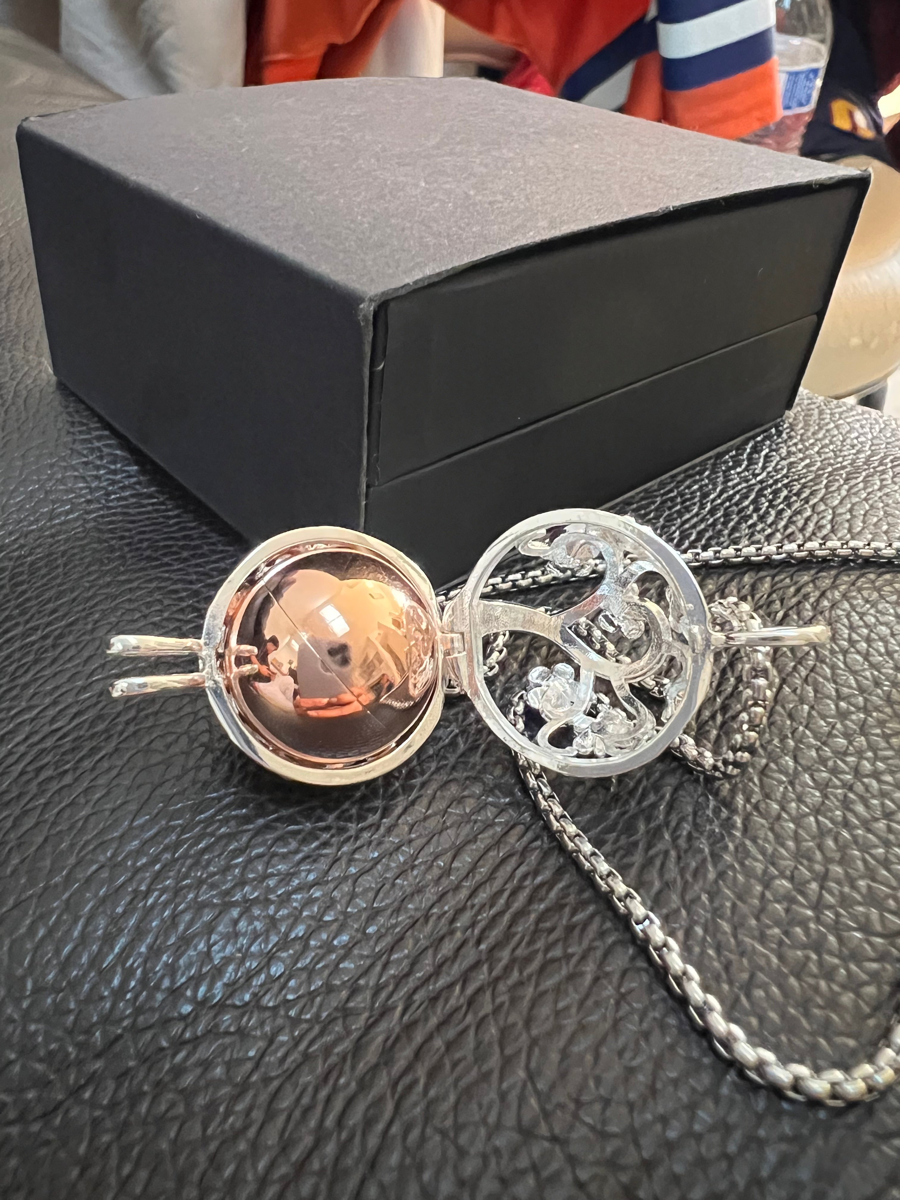 An opened up Cage of a cremation Bola Pendant with a jewelry box in the background